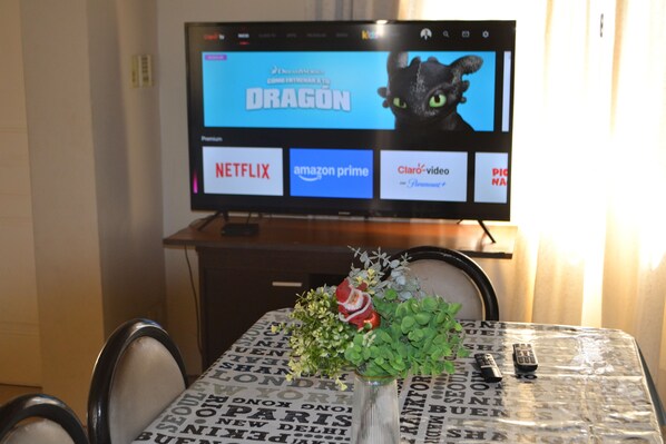 A television displaying the Netflix logo, a remote control, and a decorative vase with flowers on a table. - Amplia e iluminada casa en Mendoza (Mendoza)