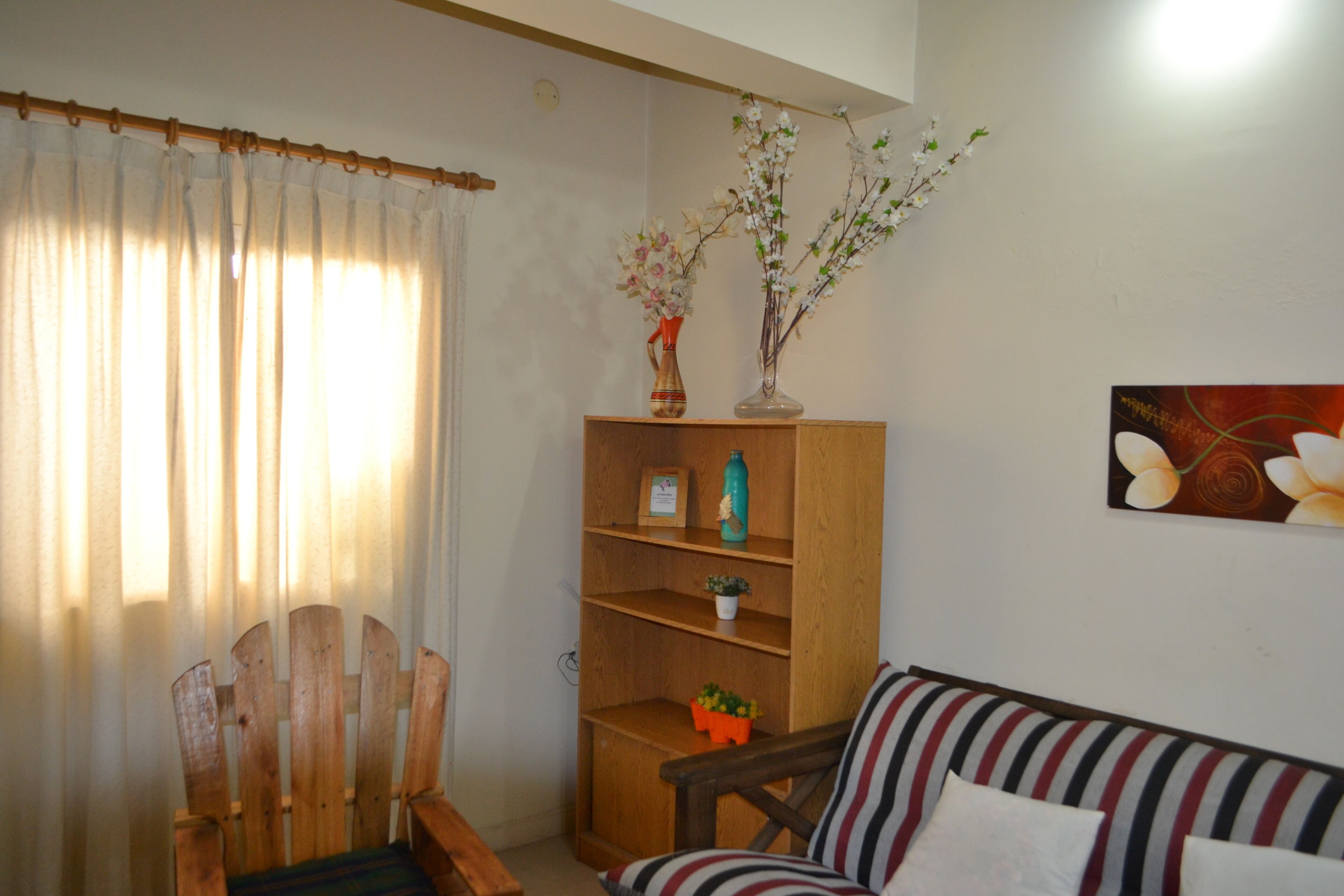 A living room with a wooden chair, a striped sofa, a wooden bookshelf, and a painting on the wall.