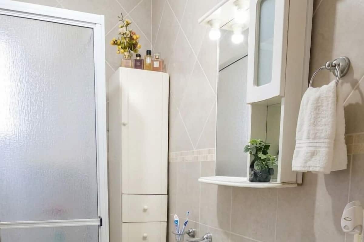 A bathroom with a shower, sink, mirror, towel rack, and storage cabinets.