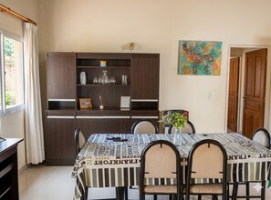 Uma área de refeições com uma mesa posta para seis, um armário com copos e um quadro abstrato colorido na parede.