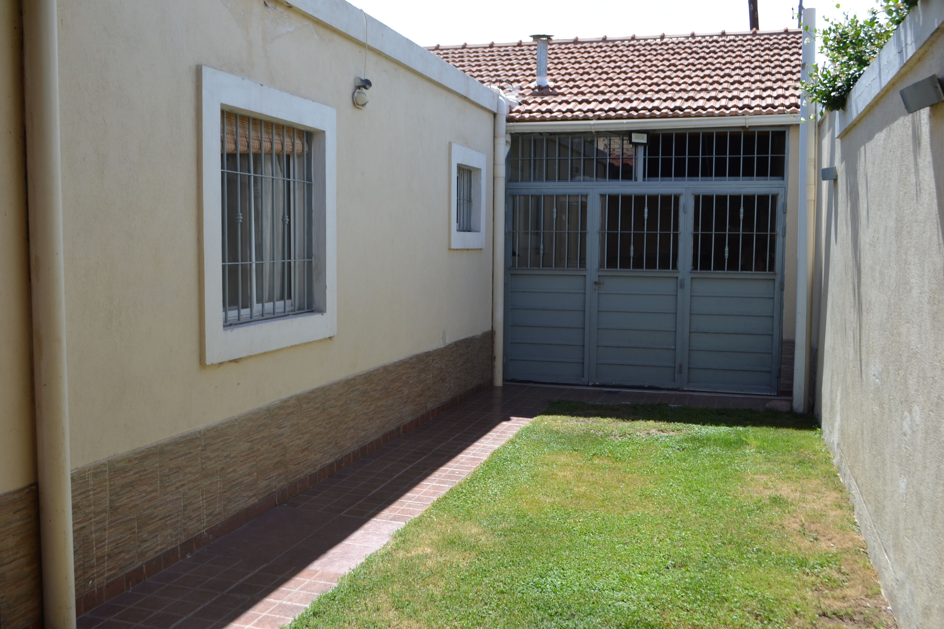 A small, enclosed outdoor area with a paved walkway, a grassy patch, and a garage door.