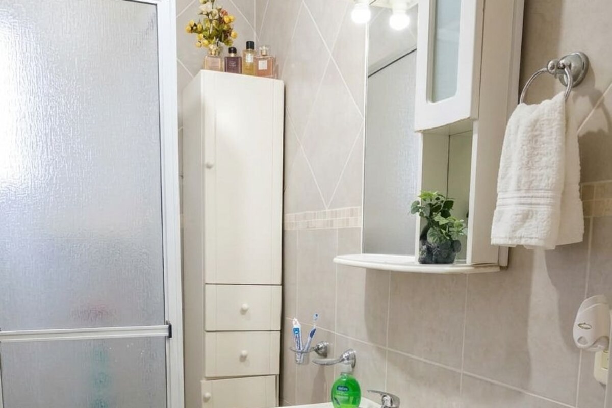 A bathroom with a shower, sink, mirror, towel rack, and storage cabinets.