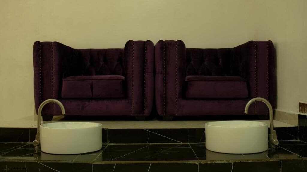 A bathroom with two sinks and a dark purple upholstered bench.