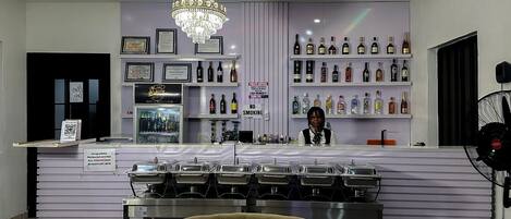 A bar area with a counter, shelves of liquor bottles, a chandelier, and a 'No Smoking' sign.
