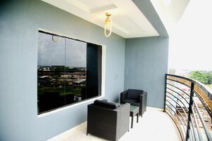 A balcony with a large window, a black sofa, a wicker chair, and a railing.