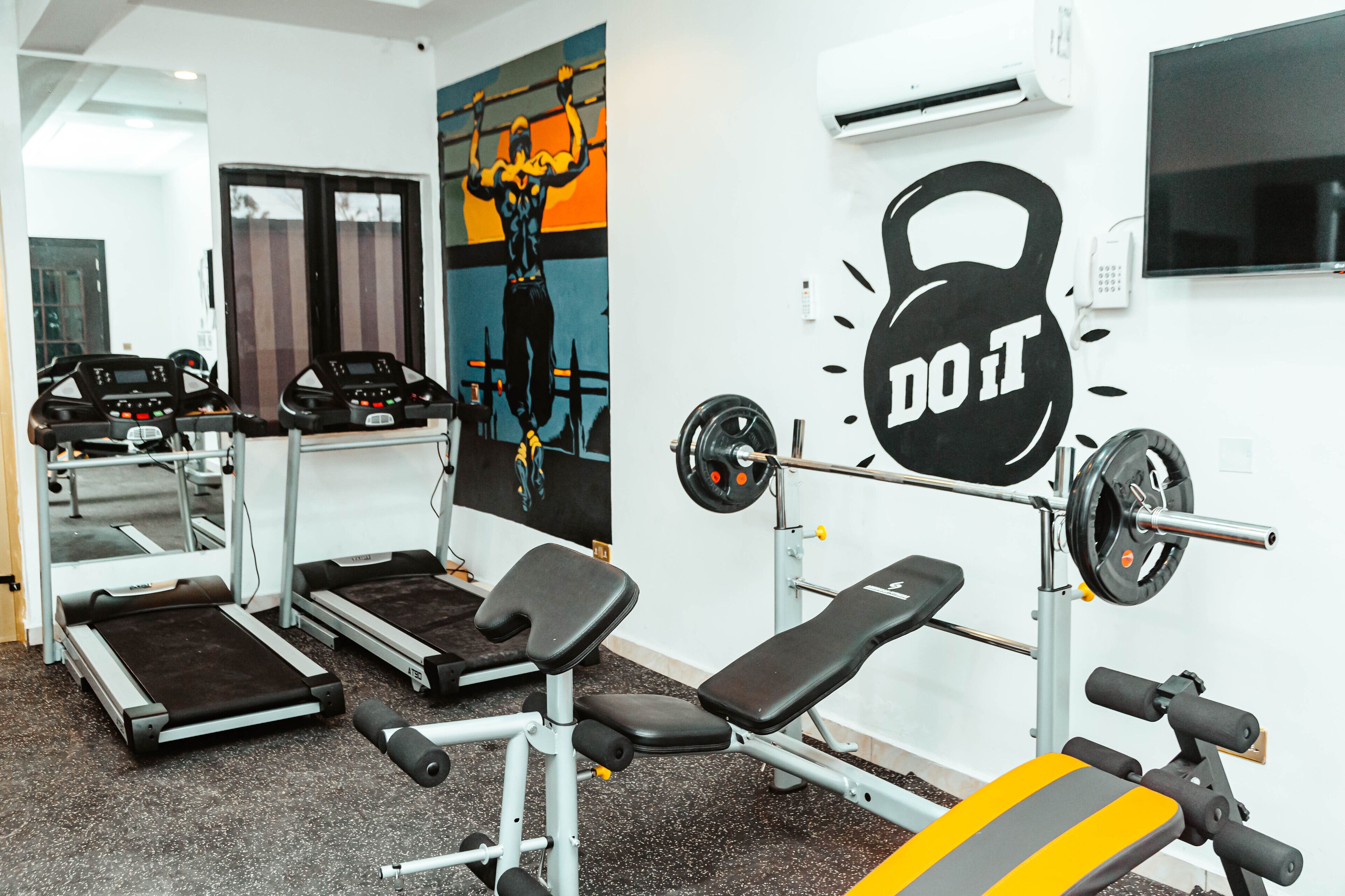 A gym with treadmills, weight benches, and a wall-mounted kettlebell.