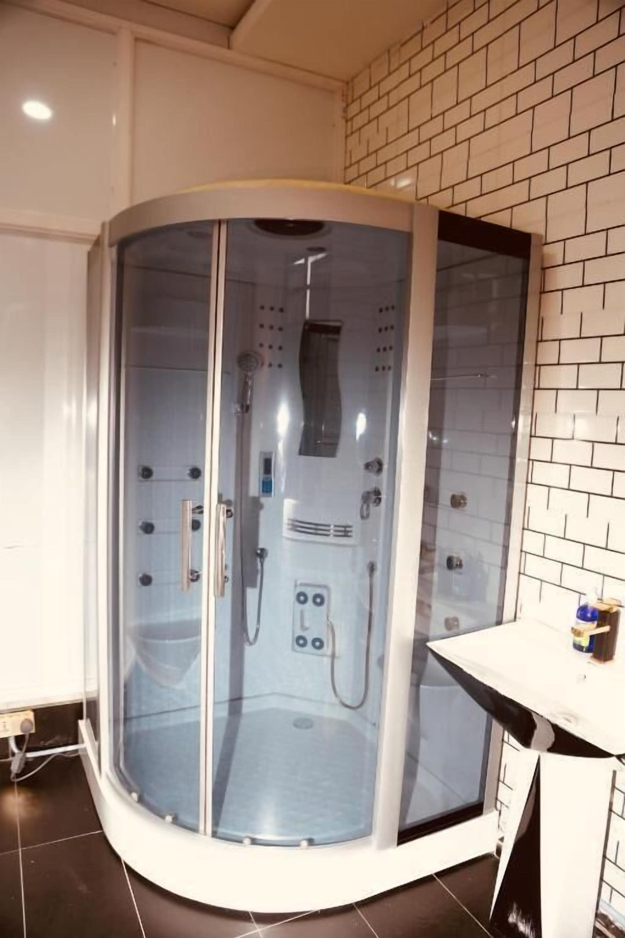 A glass-enclosed shower room with control panels and a handheld showerhead.