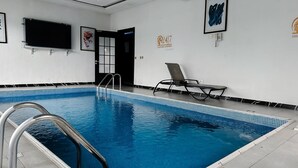 Une piscine intérieure à l’eau d’un bleu cristallin, avec une échelle en métal et un fauteuil de relaxation.