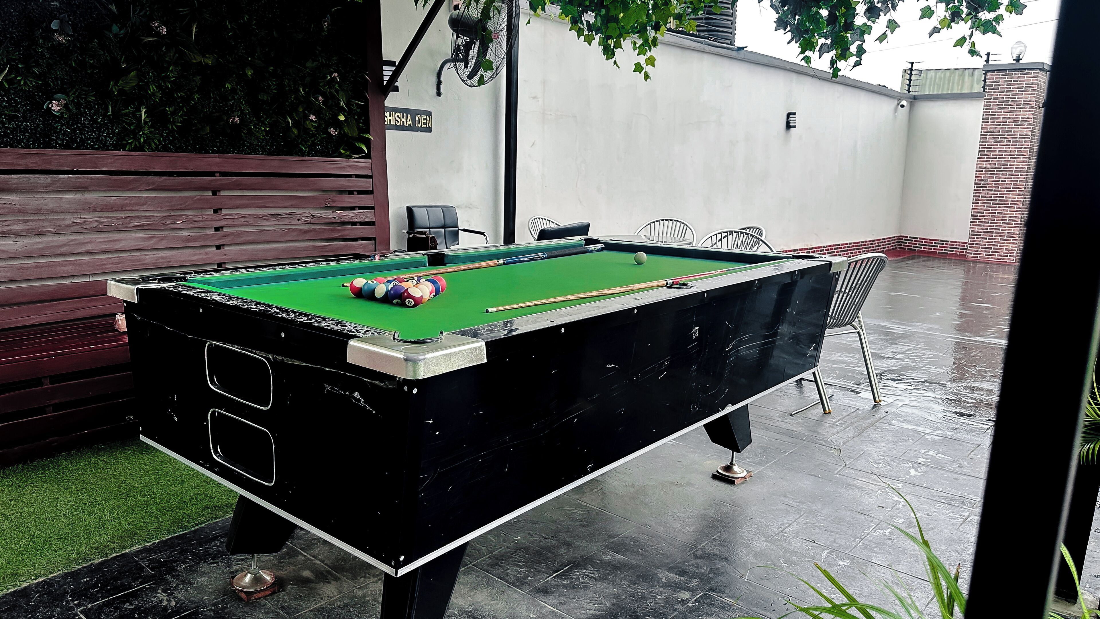 A pool table with balls, a bench, and a fan.