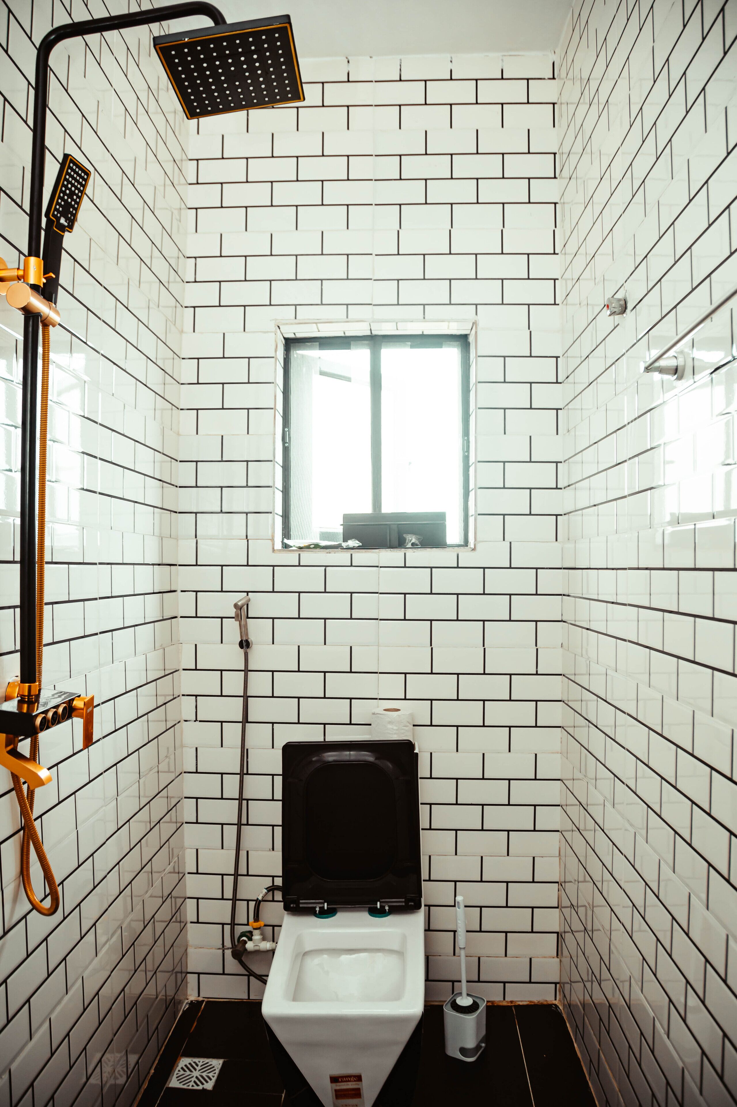 Une petite salle de bain carrelée, équipée de toilettes, d’une fenêtre et d’une douche.