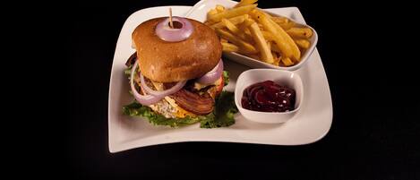 Un plato que incluye una hamburguesa con lechuga, queso y una loncha de tocino, acompañado de papas fritas y un tazón pequeño de kétchup.