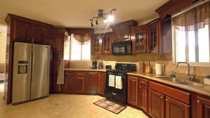 A kitchen with wooden cabinets, a stainless steel refrigerator, a microwave, a stove, and a sink.