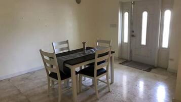 Zona de menjador amb una taula i quatre cadires, una porta amb finestre i un sòl de rajola.