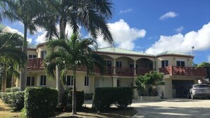 A two-story building with a red balcony, palm trees, and a clear blue sky.