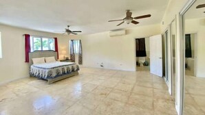 A spacious bedroom with a large bed, two ceiling fans, and a sliding glass door leading to a bathroom.