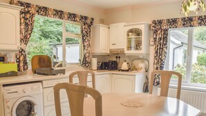 A compact kitchen with a washing machine, dining table, chairs, and a refrigerator.