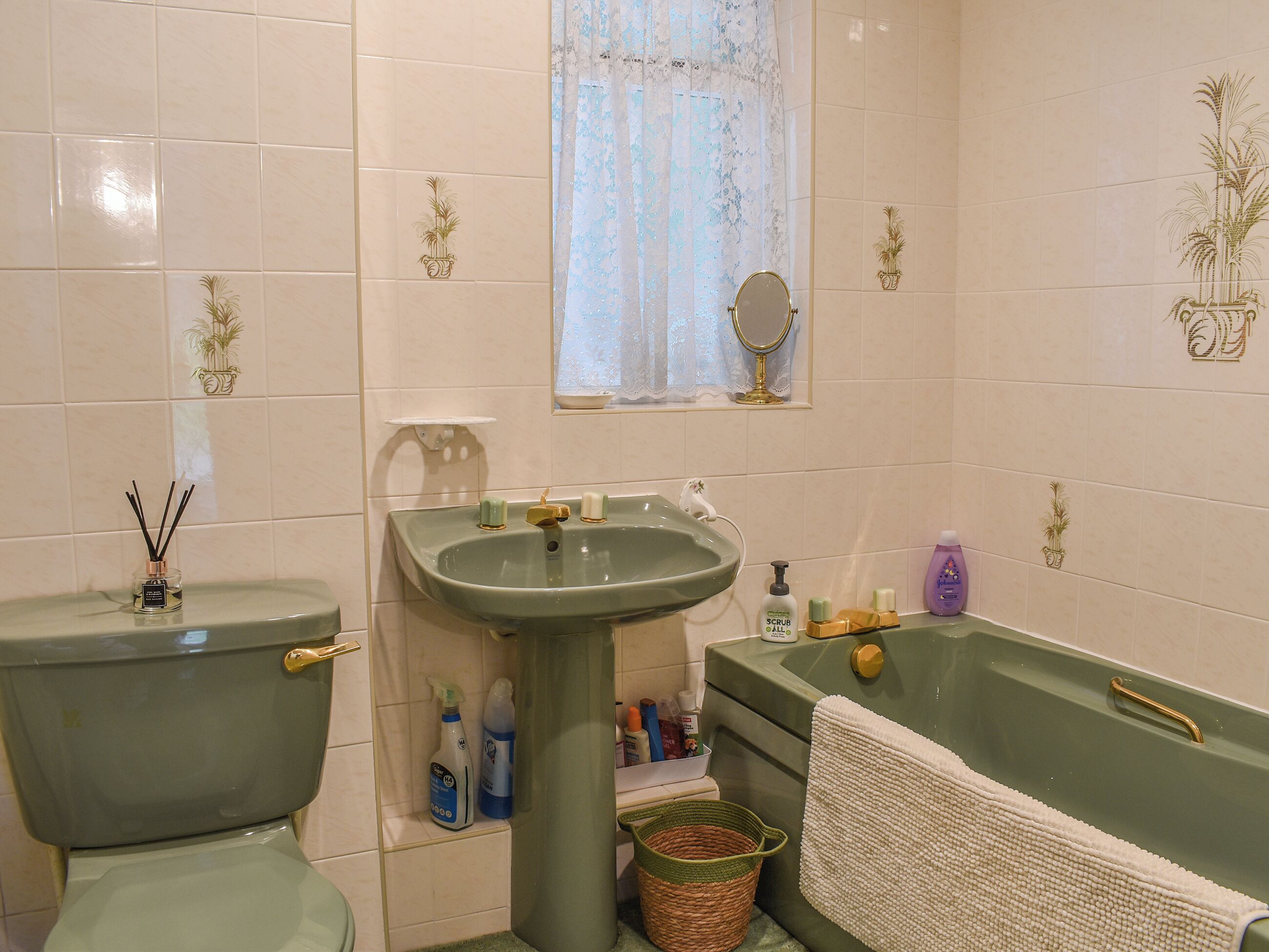 Une salle de bain avec des toilettes, un lavabo et une baignoire. On trouve des articles de toilette sur le lavabo et un panier à côté de la baignoire.