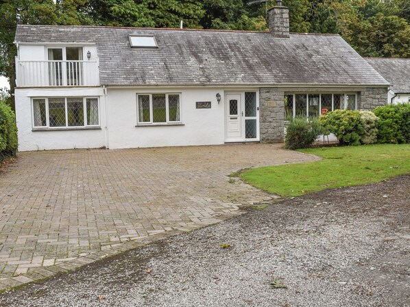A two-story white house with a stone chimney, a paved driveway, and a well-maintained lawn.