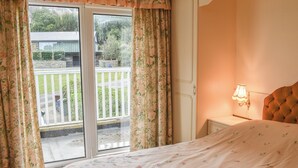 A bedroom with a bed, a nightstand, a lamp, and a sliding glass door leading to a balcony.