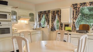 A vintage kitchen with white cabinets, a microwave, a toaster, and a dining table with floral chairs.