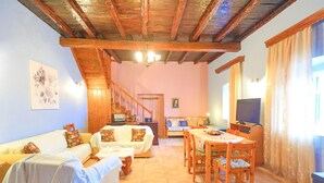 Un accogliente soggiorno con soffitto in legno, un divano, un tavolo da pranzo con sedie, una televisione e una scala che conduce a un'altra stanza.