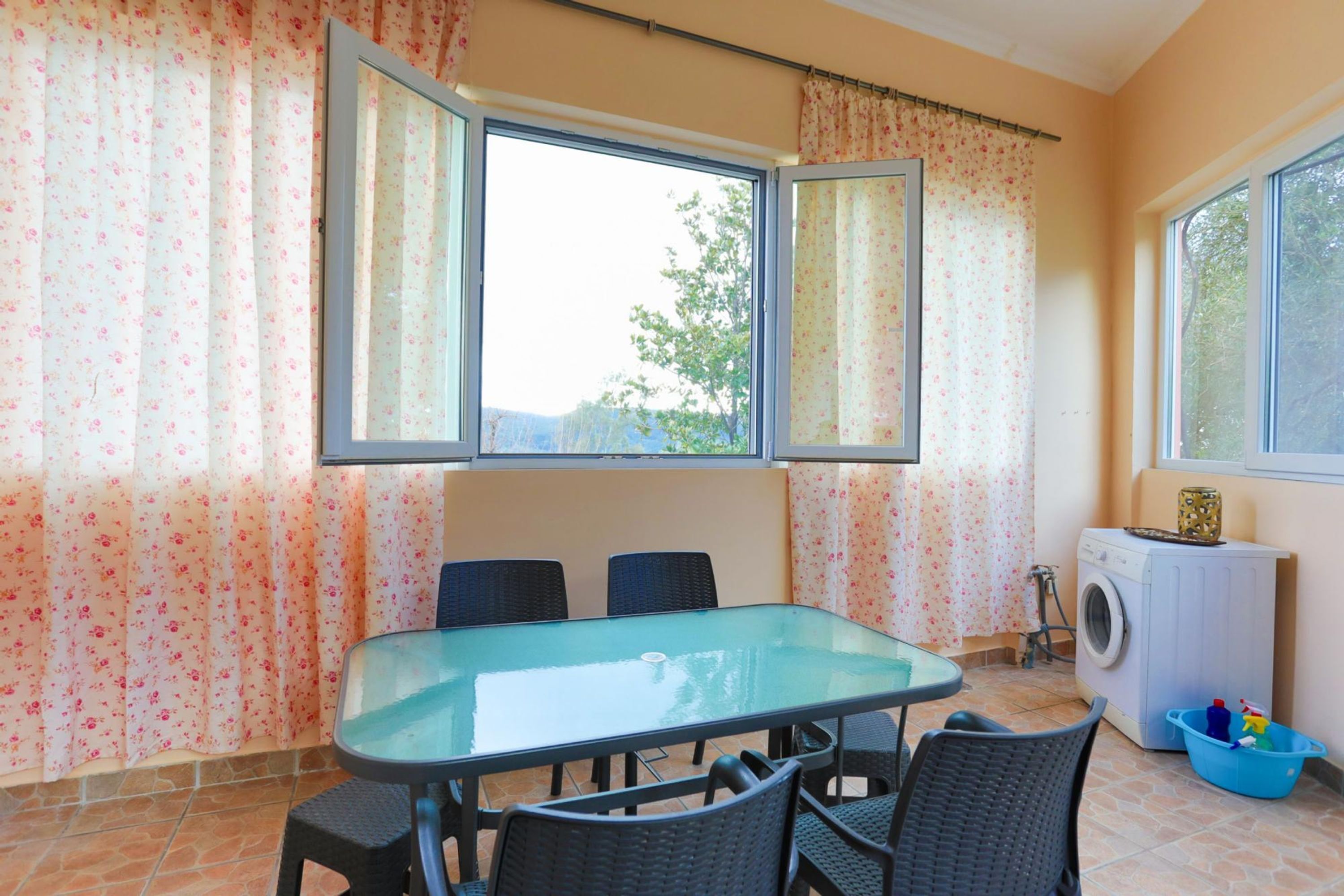 Un comedor con una mesa y sillas de vidrio, una lavadora y un cesto de ropa azul.