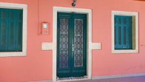 Facciata di un edificio con parete rosa, una porta verde con una finestra e una piccola finestra con persiane verdi.