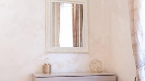 Una habitación minimalista con un aparador de color claro, un espejo redondo pequeño y un adorno encima.