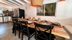A modern kitchen with a dining area, featuring a large wooden table, black chairs, and a hanging wicker light fixture.