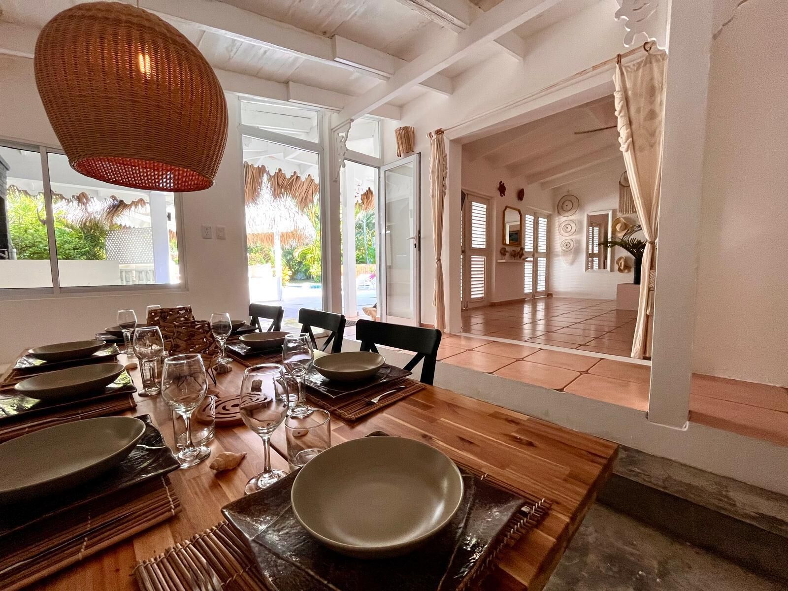 A dining area with a wooden table set for a meal, large windows, and a view of the outdoors.