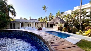 A resort pool area with a wooden deck, lounge chairs, and thatched umbrellas.