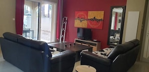 A living room with a sofa, armchairs, a coffee table, a TV, and a red wall with artwork.