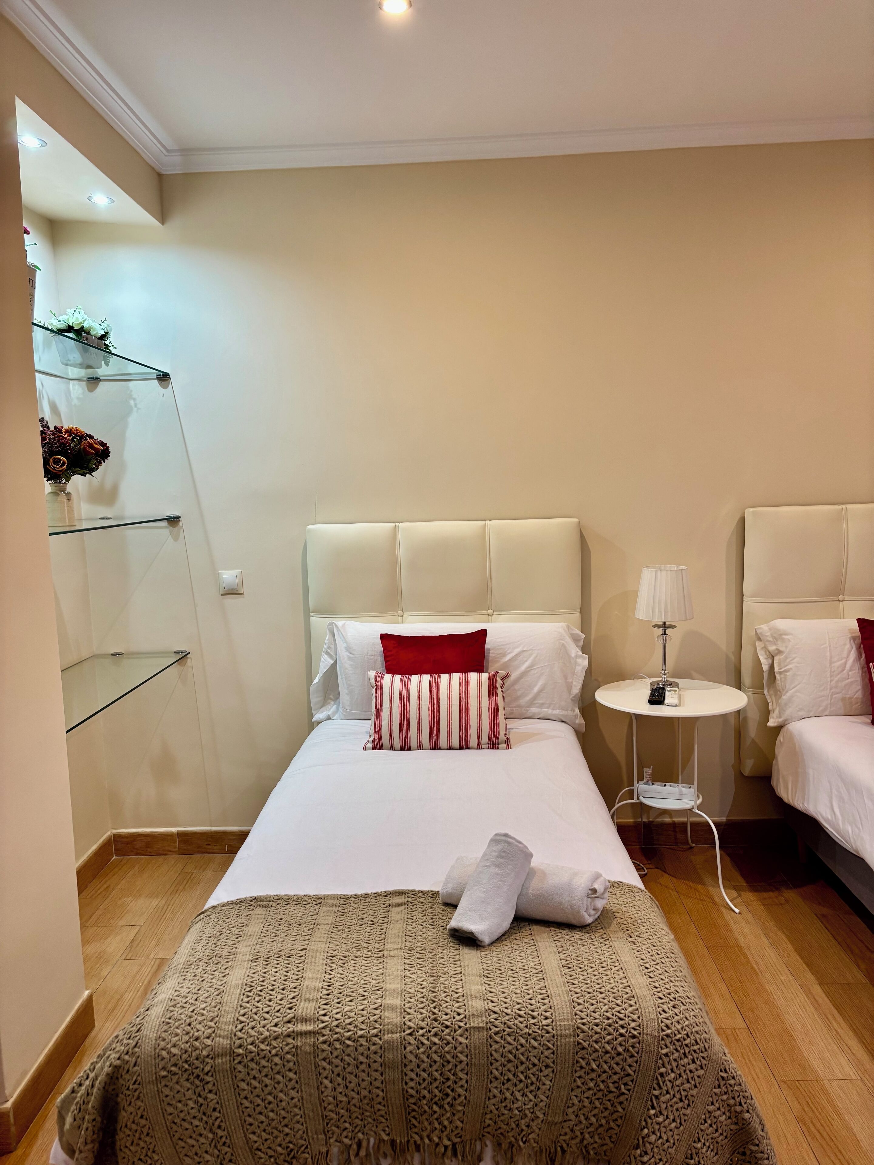 Ein Hotelzimmer mit einem Bett, einem Nachttisch mit Lampe, einer kleinen Ablagefläche mit Dekoration und einem Holzboden.