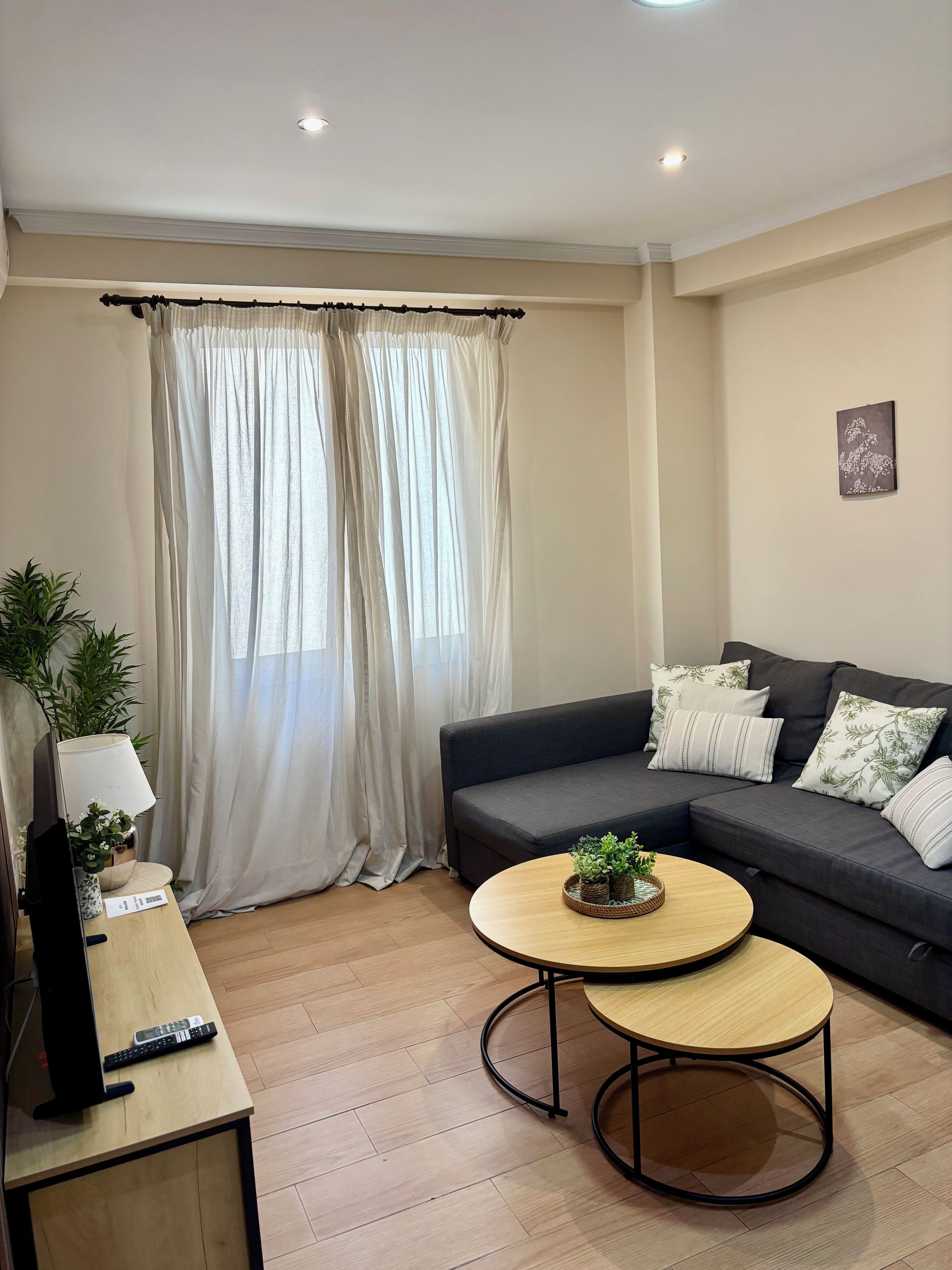 Una sala de estar moderna con un sofá gris oscuro, una mesa de centro redonda de madera y un televisor sobre un mueble de madera.