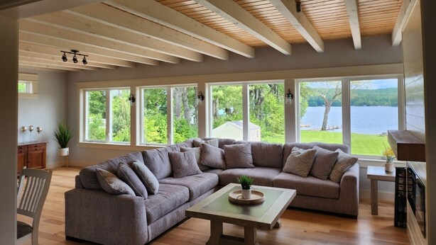 Un salón amplio con un sofá modular grande, una mesa de centro de madera y vistas a un lago a través de amplias ventanas.