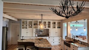 Una cocina amplia con una isla central, armarios blancos y una lámpara original.