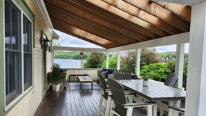 Una terraza techada al aire libre con una mesa y sillas de madera, un banco y vistas a un lago.