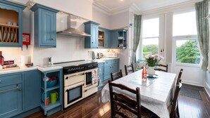 Une cuisine avec des meubles de rangement bleus, un plan de travail blanc, une cuisinière et une table à manger avec des chaises.