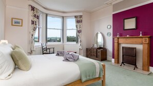 Une chambre à coucher avec un grand lit, une commode en bois, une cheminée et une vue sur l’extérieur.