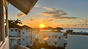 A view of a coastal residential area with white buildings, a stone wall, and a sunset over the sea. - Beach Condo in Negril Jamaica (Negril)