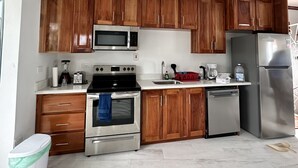 A modern kitchen with wooden cabinets, stainless steel appliances, and a tiled floor. - Beach Condo in Negril Jamaica (Negril)