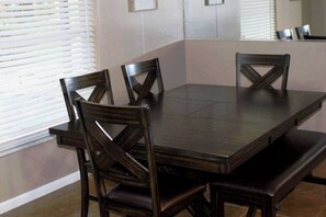A rectangular dining table with four chairs, a bench, and a window with blinds.