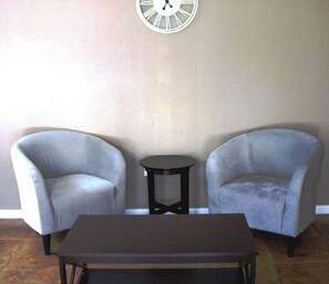 A room with two armchairs, a small round table, and a rectangular table.