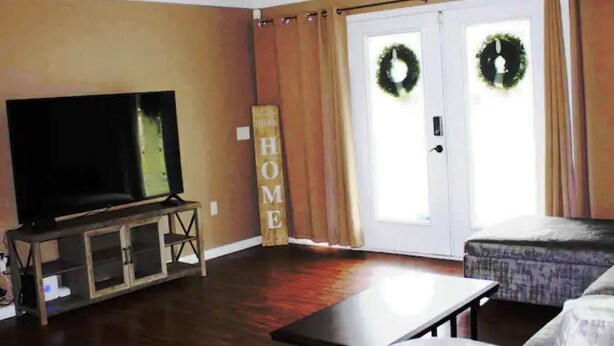 Un salon avec un téléviseur, un canapé, une table basse et un panneau décoratif portant l’inscription « HOME ».