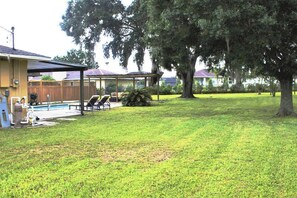 A backyard with a swimming pool, lounge chairs, and a covered patio area.
