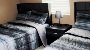 Une chambre à coucher avec deux lits, chacun doté de draps à rayures, une table de chevet avec une lampe et un tiroir.