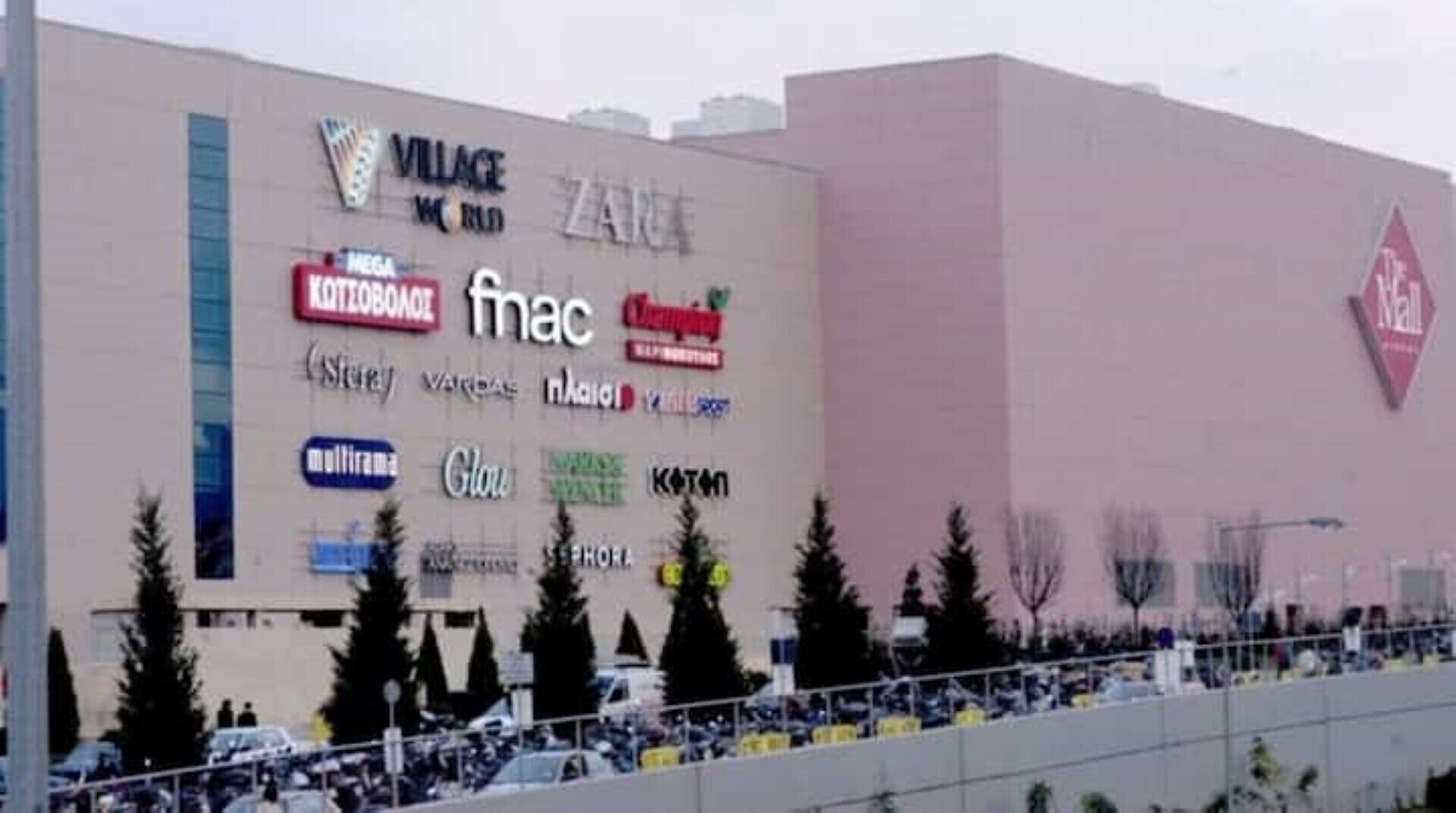Un immeuble dont la façade est ornée de nombreux logos de commerces, notamment ceux de Village World, ZARA et KOTOBUKI.