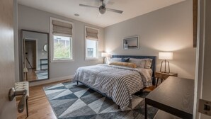 Un dormitorio con una cama, dos lámparas de noche, un ventilador de techo y una ventana con persianas.