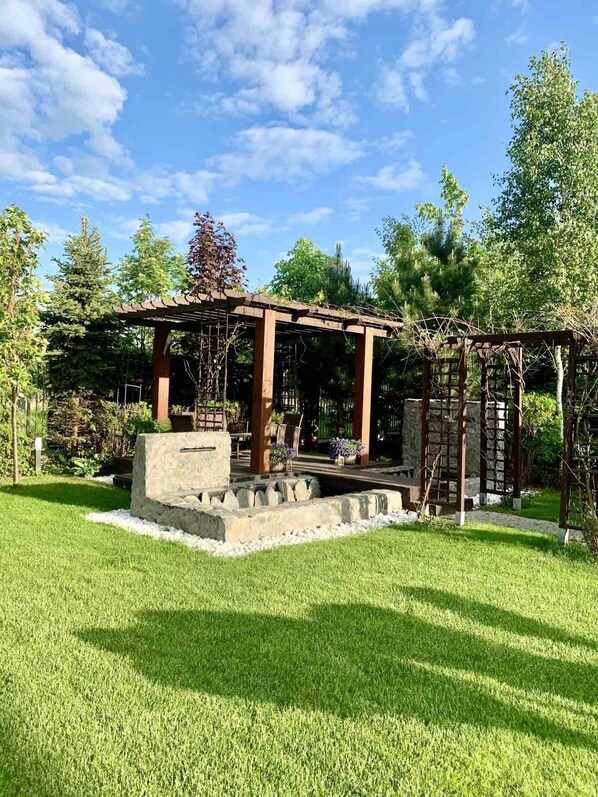 A gazebo with a stone base and wooden beams, surrounded by a well-maintained lawn and trees. - Luxury Villa - JessApart Walendia (Nadarzyn)
