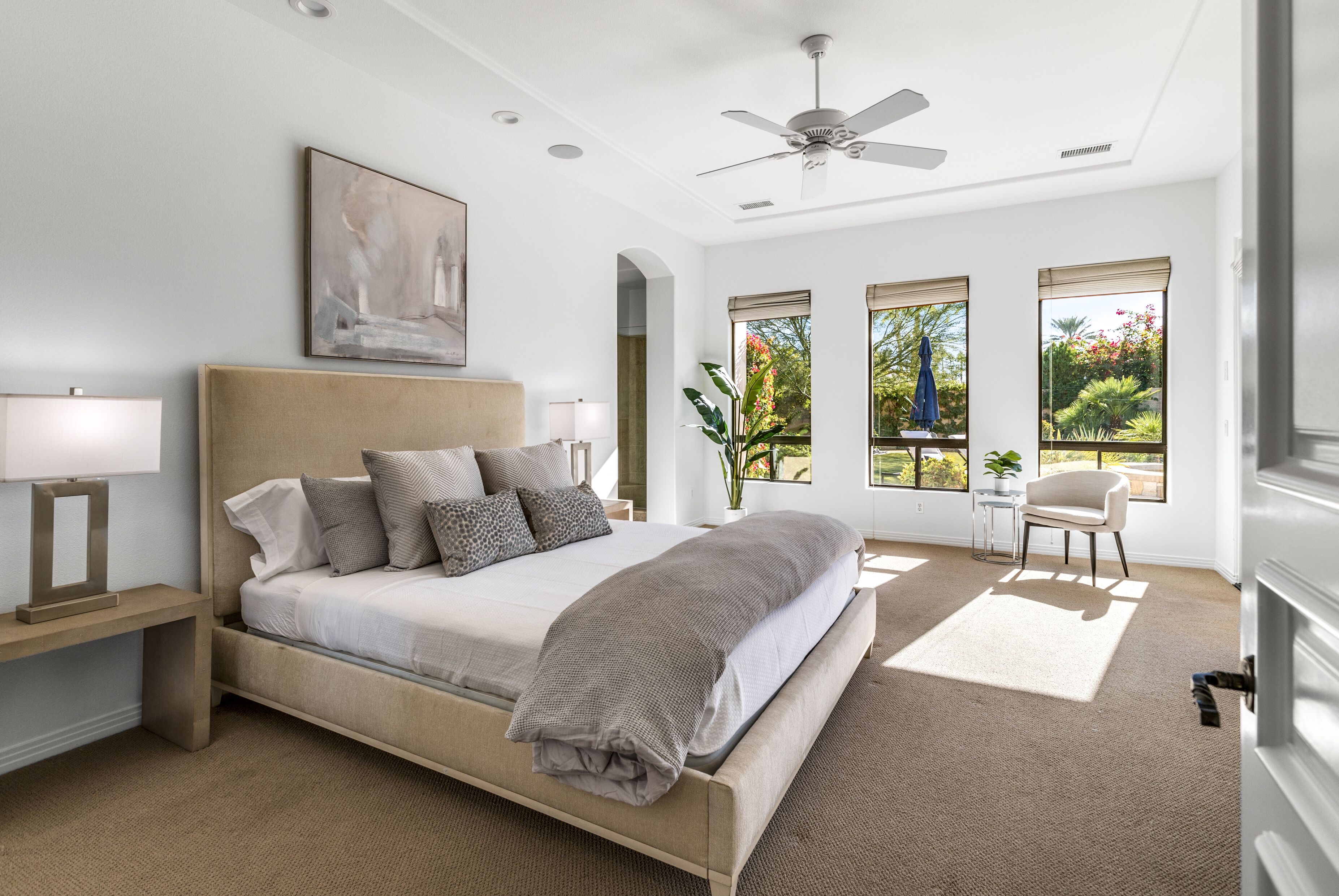 A bedroom with a large bed, a ceiling fan, and a view of the outdoors through the windows.